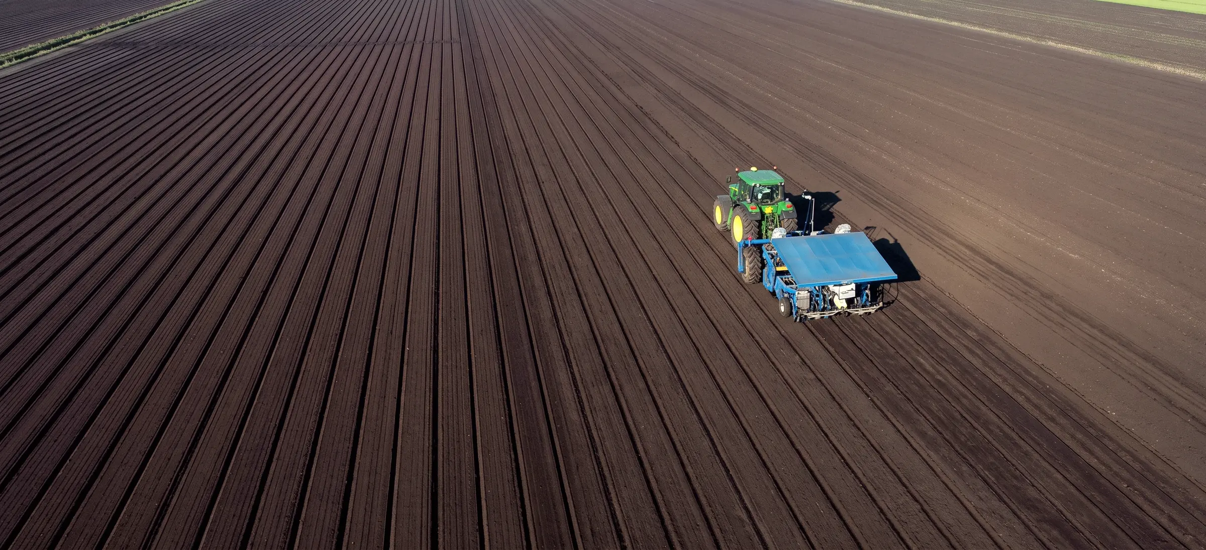 Aerial view of a Hundley Farms tractor working freshly plowed rows of dark muck soil